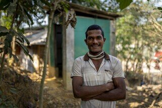 Md Zakir smiles with his hands crossed standing comfortably as there is no bad smell in front of a community toilet in the refugee camp. (Mushfiqul Alam/Oxfam)