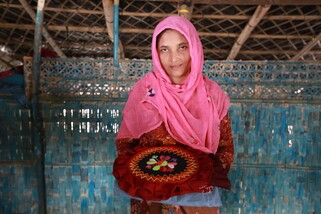 Senowara Begum smiles while holding her stitched product with a design in her home. (Jubayer Bin Iqbal/Oxfam)