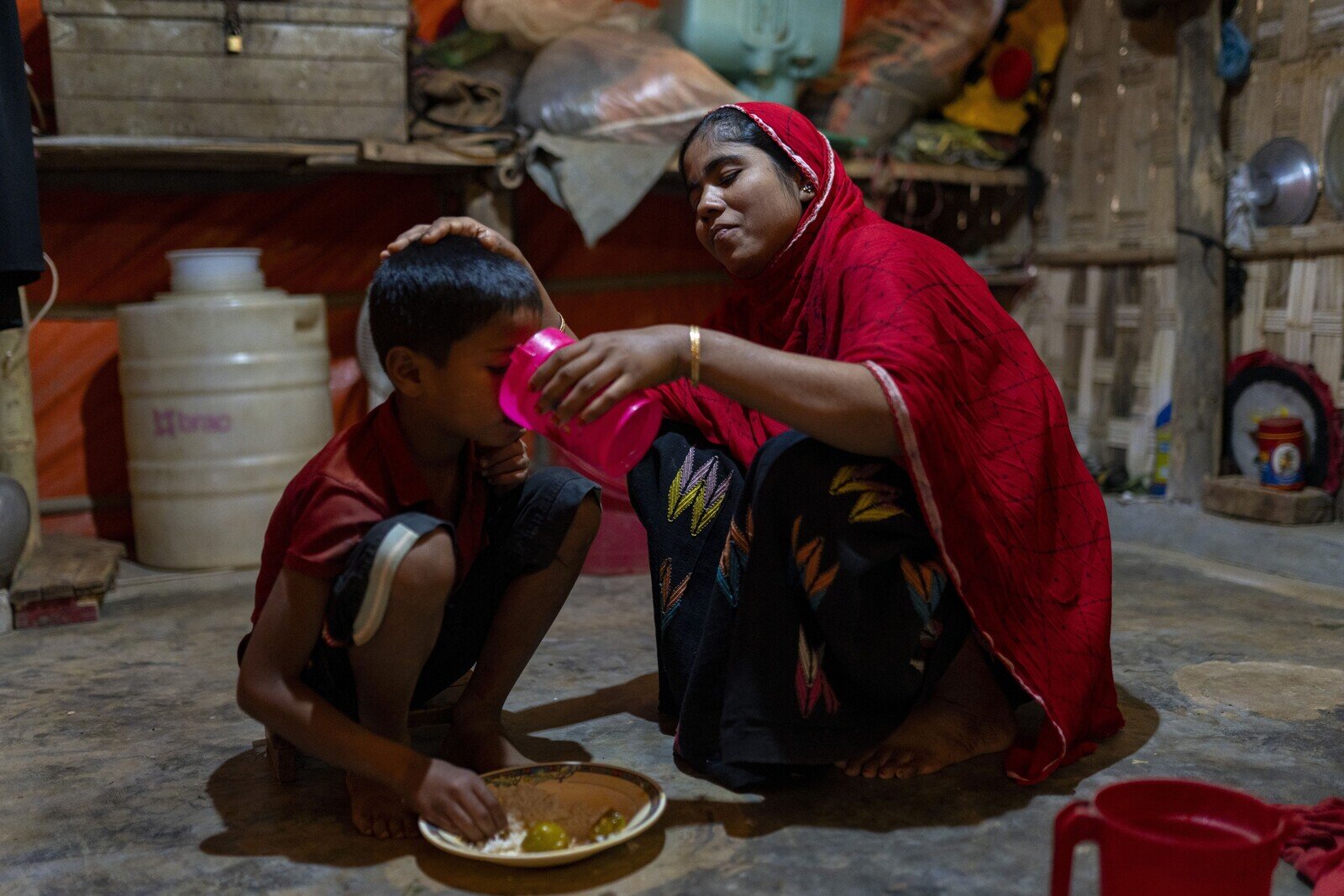 Khaleda takes care of her child and helps him drink the safe water while he eats. (Mushfiqul Alam/Oxfam)