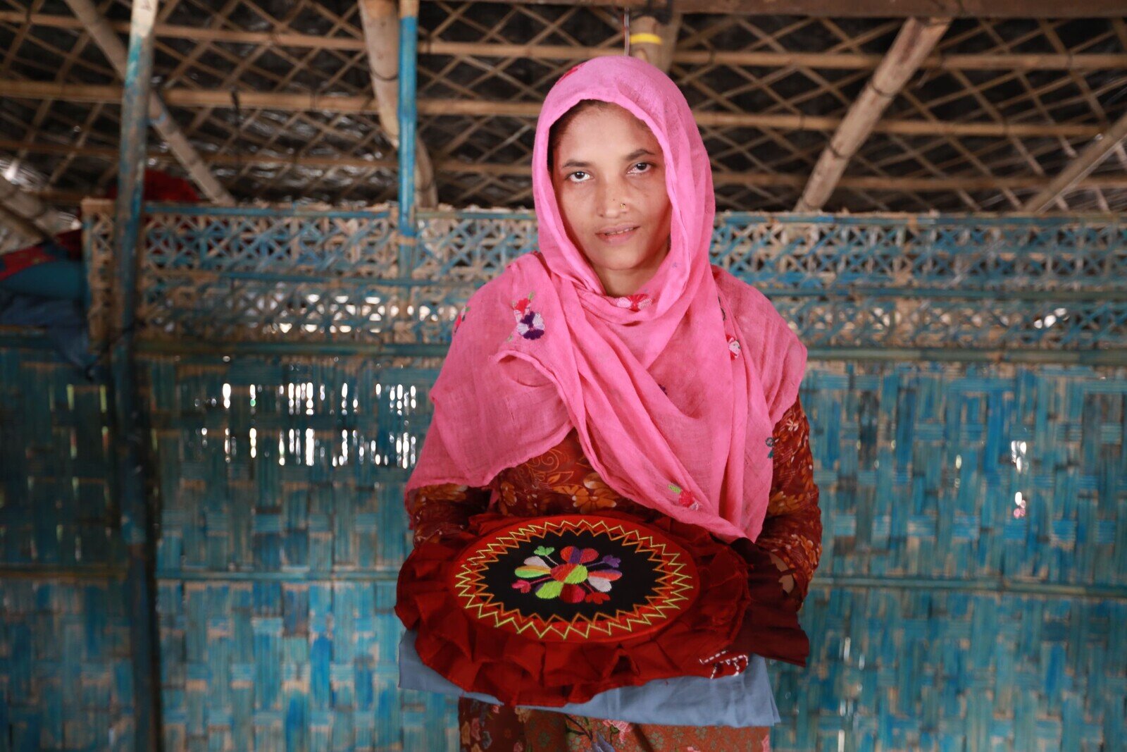 Senowara Begum smiles while holding her stitched product with a design in her home. (Jubayer Bin Iqbal/Oxfam)